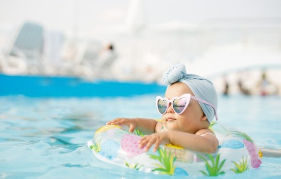 Cute funny toddler girl in colorful swimsuit and sunglasses relaxing on inflatable toy ring floating in pool have fun during summer vacation in tropical resort. Child having fun in swimming pool.