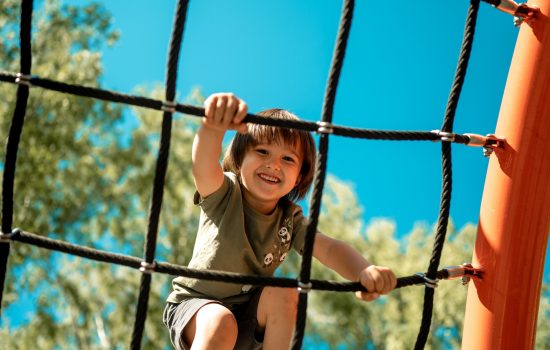A child climbs up an alpine grid in a park on a playground on a hot summer day. children's playground in a public park, entertainment and recreation for children, mountaineering training.